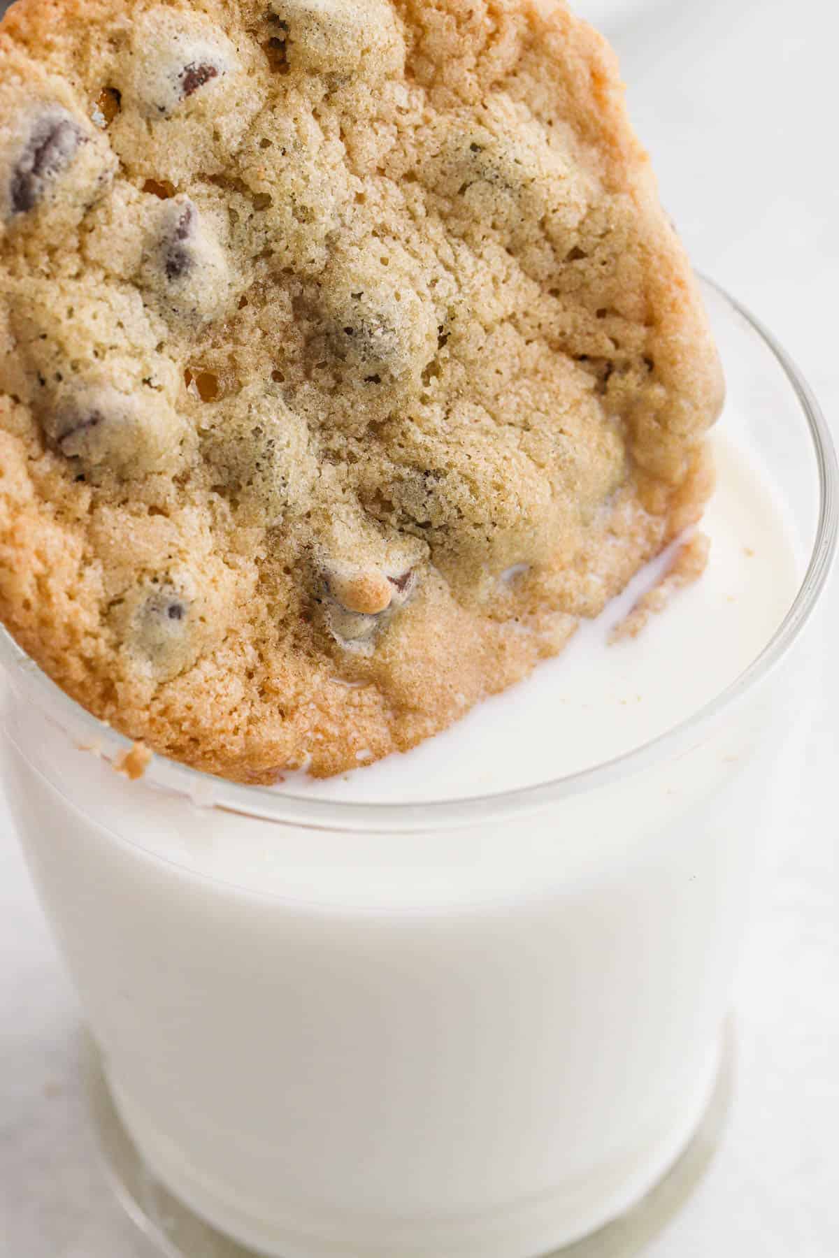 A crispy chocolate chip cookie dunking into a glass of milk.