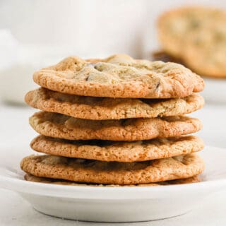 A stack of crispy chocolate chip cookies on a white plate on the table.