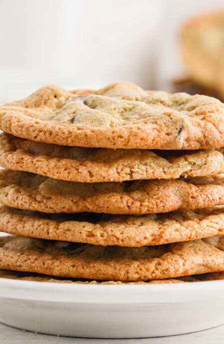 A stack of crispy chocolate chip cookies on a white plate on the table.