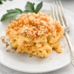 A plateful of slow cooker mac and cheese with a fork on the side a sprig of parsley.