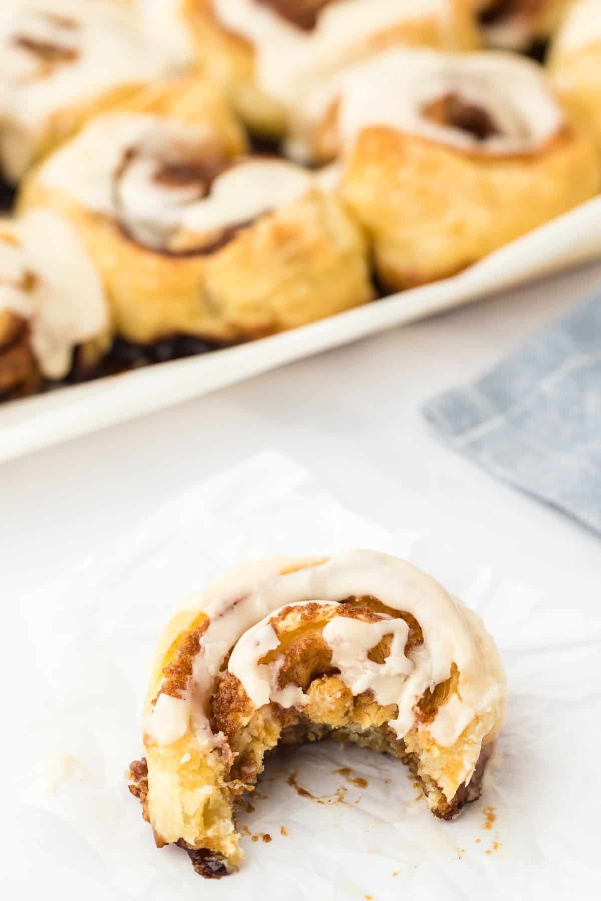 An easy cinnamon roll with a bite taken and a pan of more in the background.