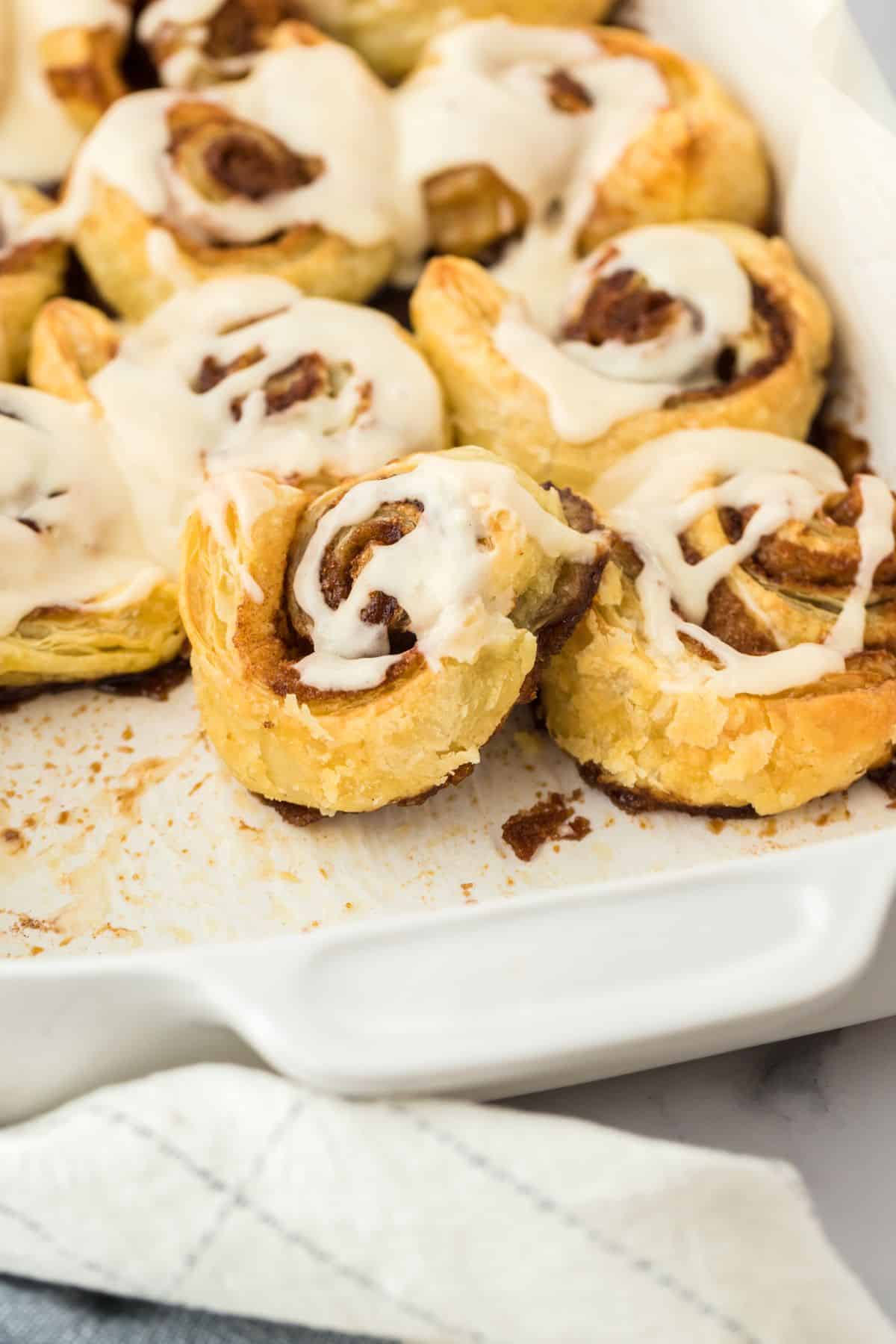 Easy cinnamon rolls in a baking dish with a few removed and a creamy icing drizzled over the top.