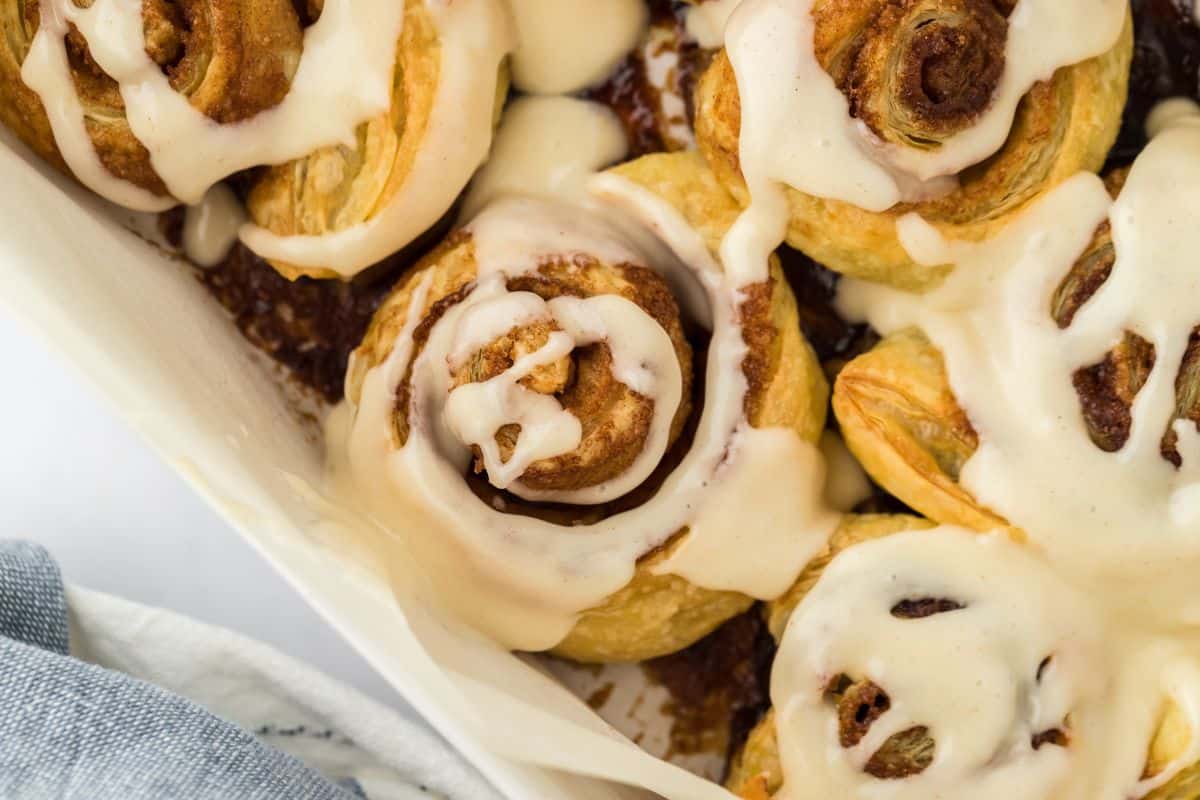 Lazy cinnamon rolls with puff pastry baked up in a white baking dish and topped with creamy icing.
