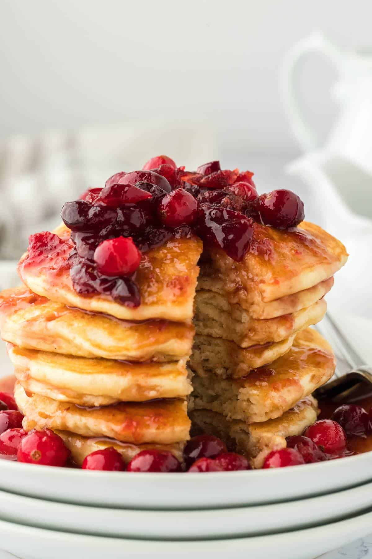 Eggnog Pancakes sitting on a white plate topped with Cranberry Maple Syrup and a fork cutting through the pancakes.