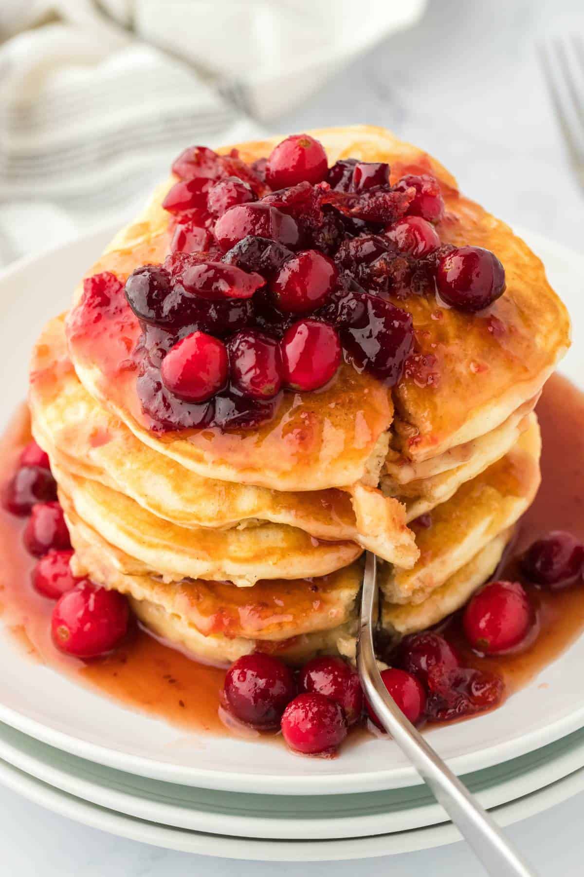 Eggnog Pancakes recipe sliced into sitting on a white plate topped with cranberries for the holiday season.