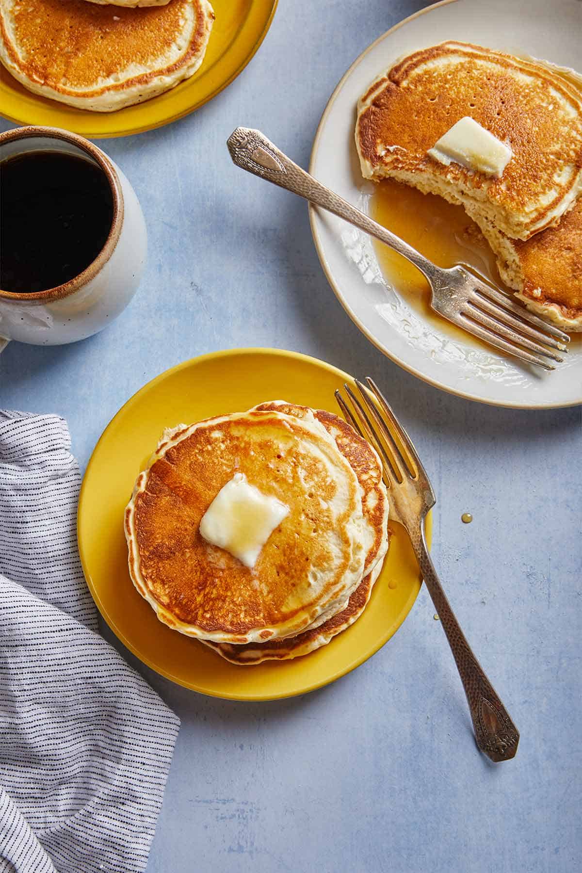 A tall stack of fluffy pancakes on a plate with a fork next to it.