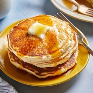 A stack of fluffy pancakes with maple syrup drizzled down the sides and a pat of butter on top.