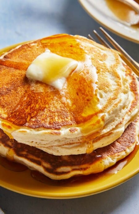 A stack of fluffy pancakes with maple syrup drizzled down the sides and a pat of butter on top.