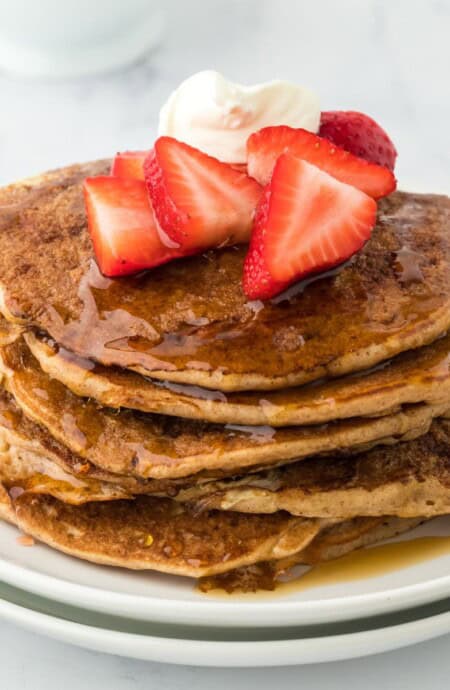 A stack of French toast pancakes on a plate with whipped cream and strawberries on top.