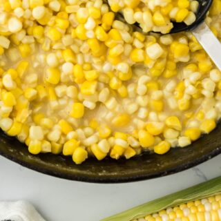 Fried Corn Recipe in a skillet being scooped on a white background