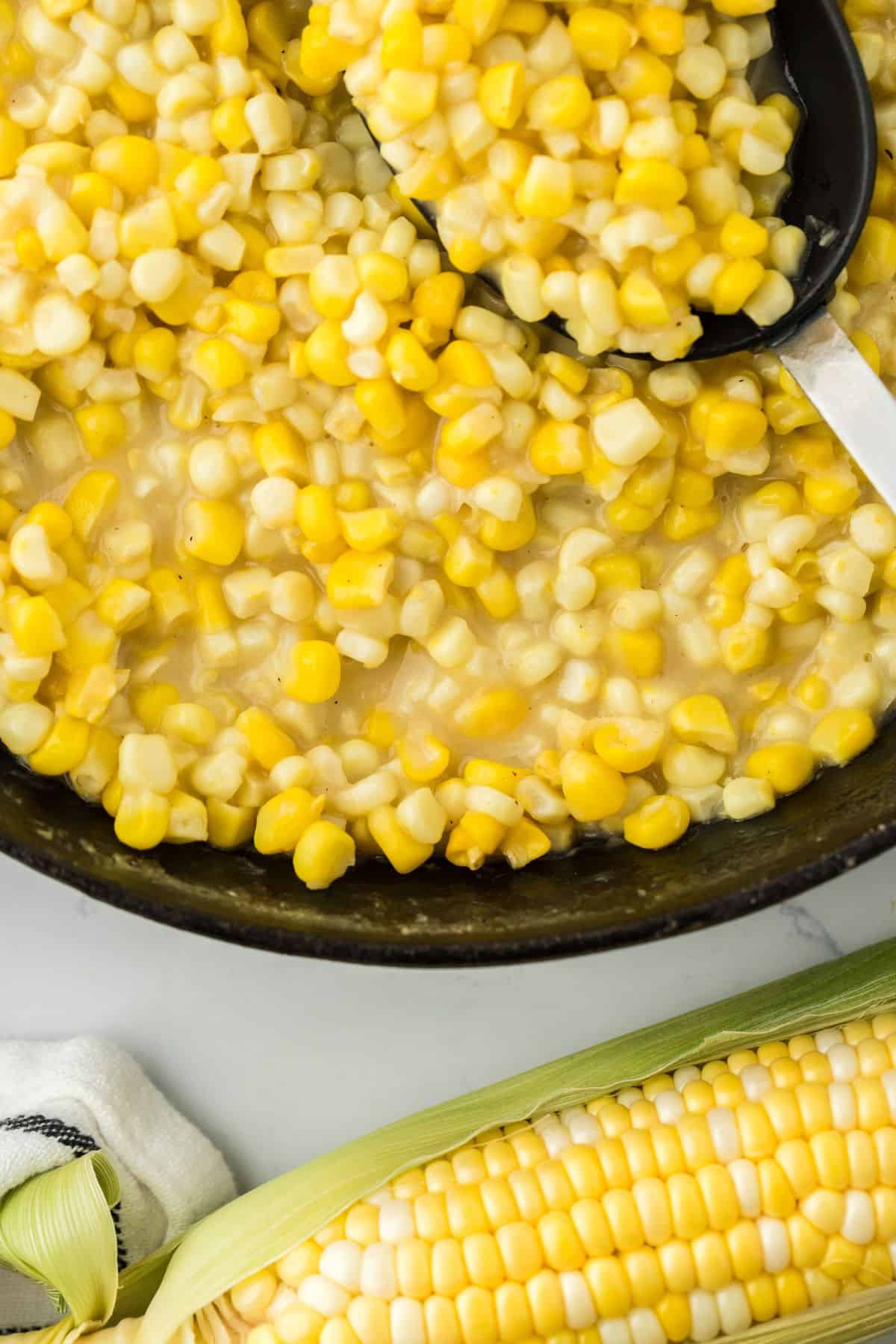 Fried corn in a black cast iron skillet with a spoon in it and an ear of corn off to the side.