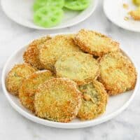 A plate of fried green tomatoes on the table with raw green tomatoes on a plate in the background.