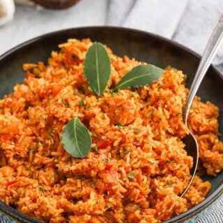 A bowl of easy jollof rice on the table with a spoon in the bowl.