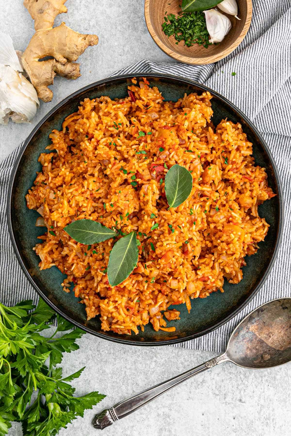 A bowl of jollof rice on the table with bay leaves on top.