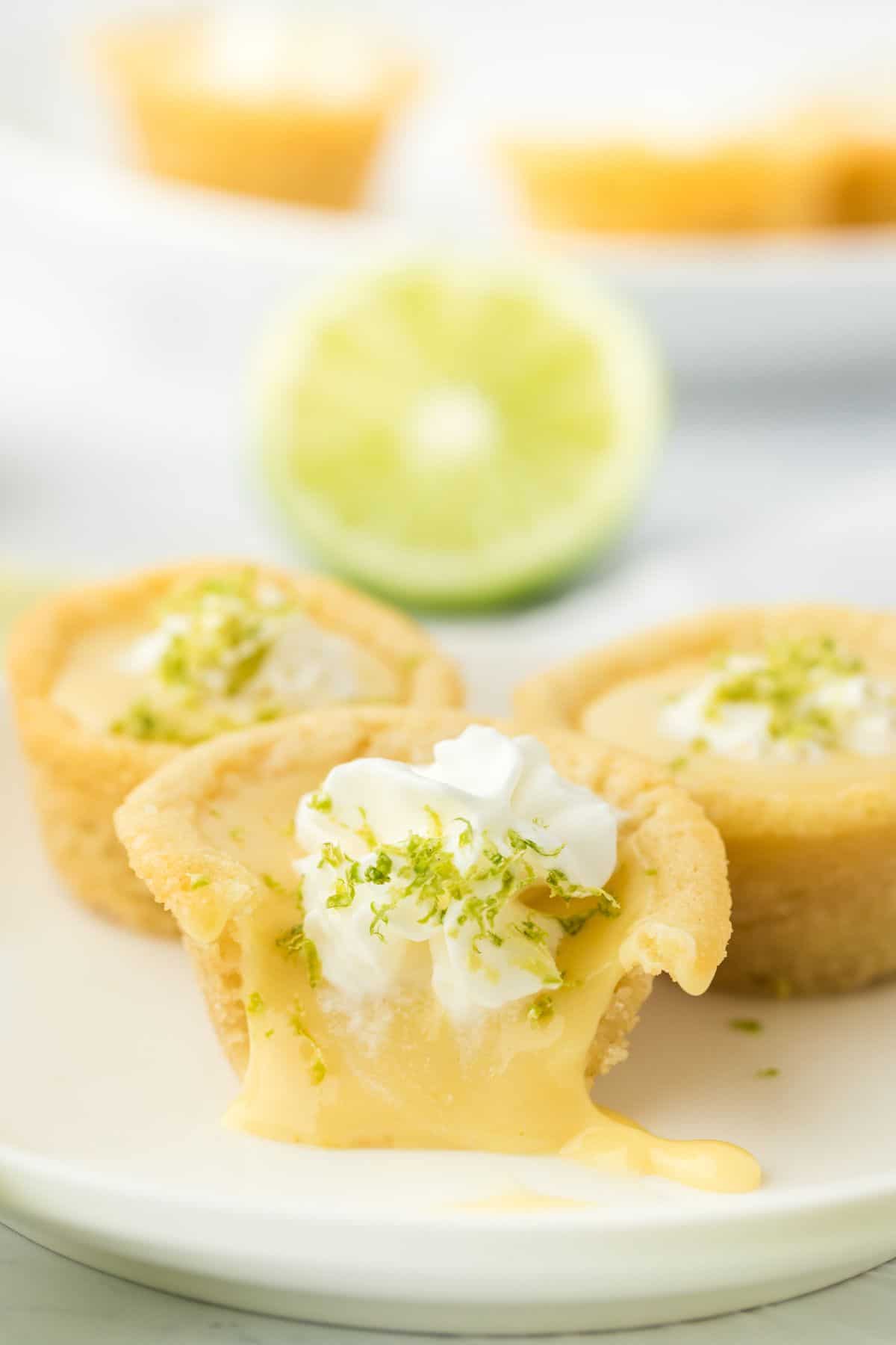 Key lime cookie cups on a plate with one bitten into and the lime filling oozing out.