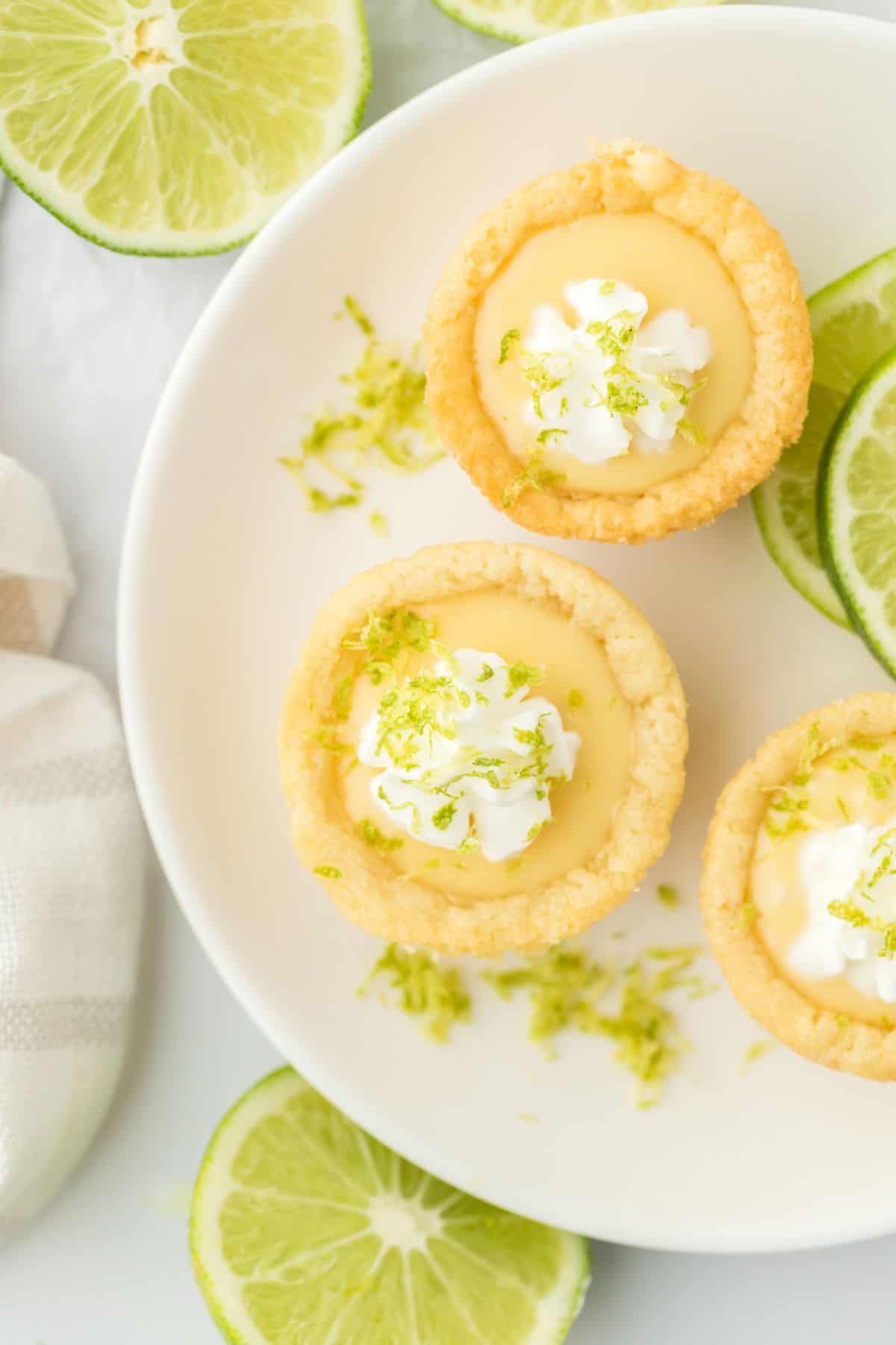 A white plate topped with key lime cookie cups and a lime half in the corners.