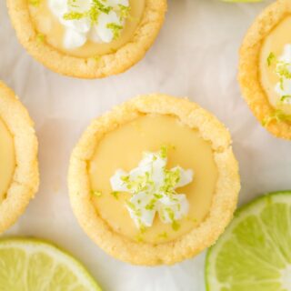 Key lime cookie cups on a white surface garnished with whipped cream and lime zest.