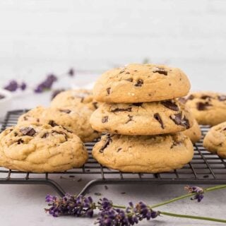 A pile of lavender chocolate chip cookies on a wire rack with some in a stack.