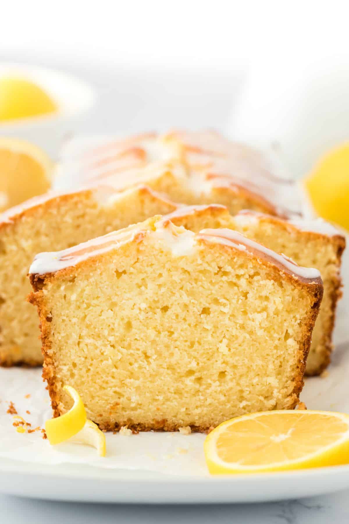 A lemon cake baked in a loaf pan facing the camera with slices cut and staggered but standing up.