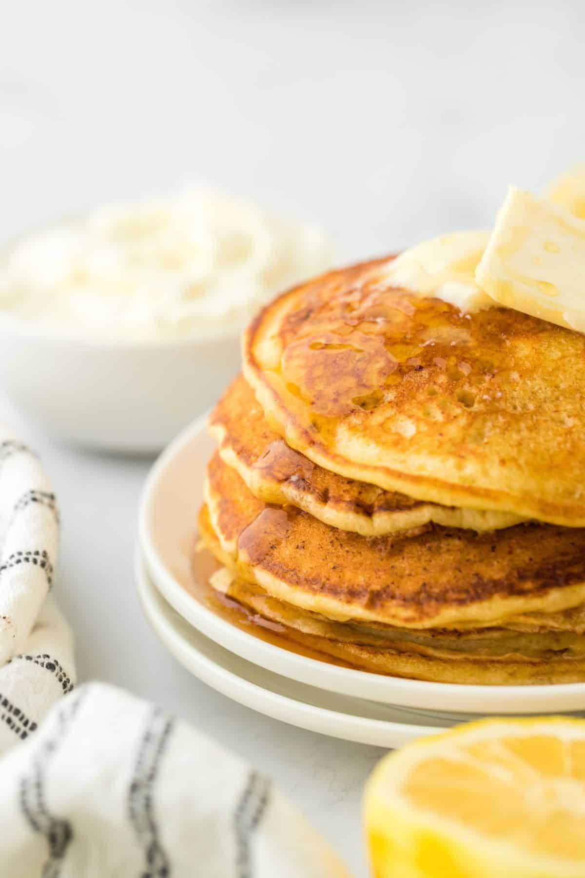 Fluffy lemon ricotta pancakes stacked high on a plate with butter and syrup being poured over them