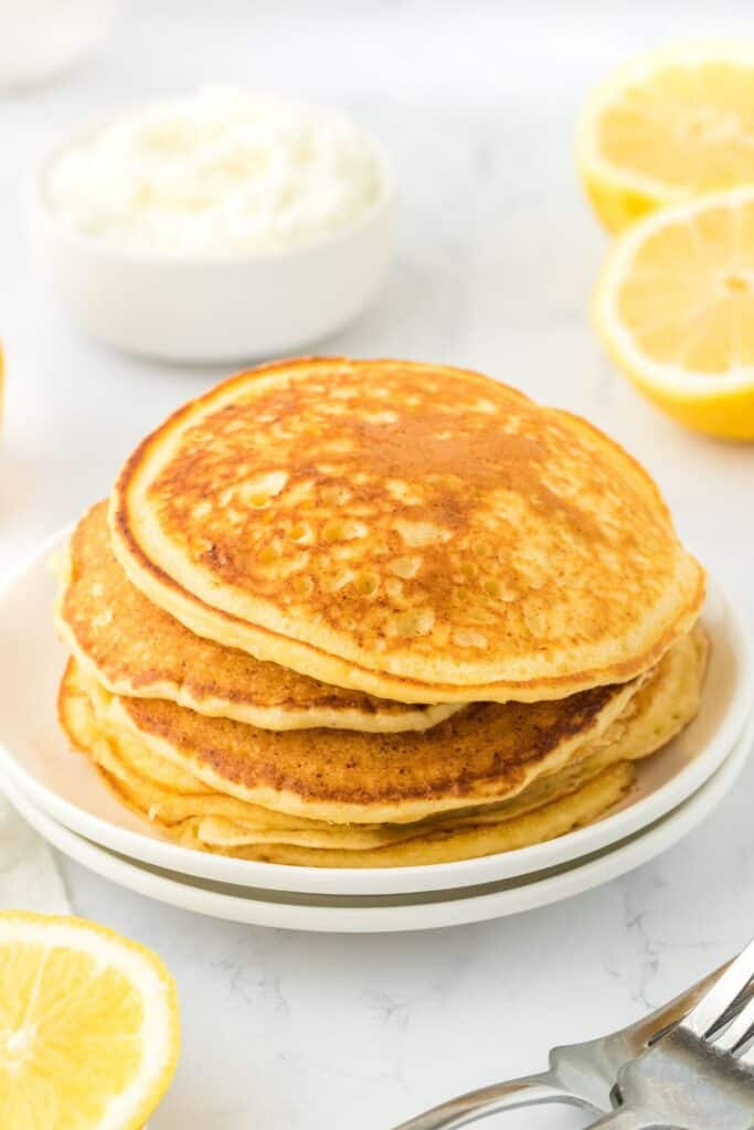 A stack of Lemon Ricotta Pancakes topped with butter and served on a blue and white plate with a fork