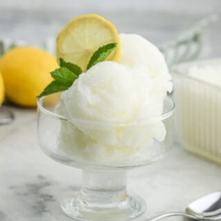 A glass dish of lemonade sorbet on the table with a piece of lemon slice and fresh mint for garnish.