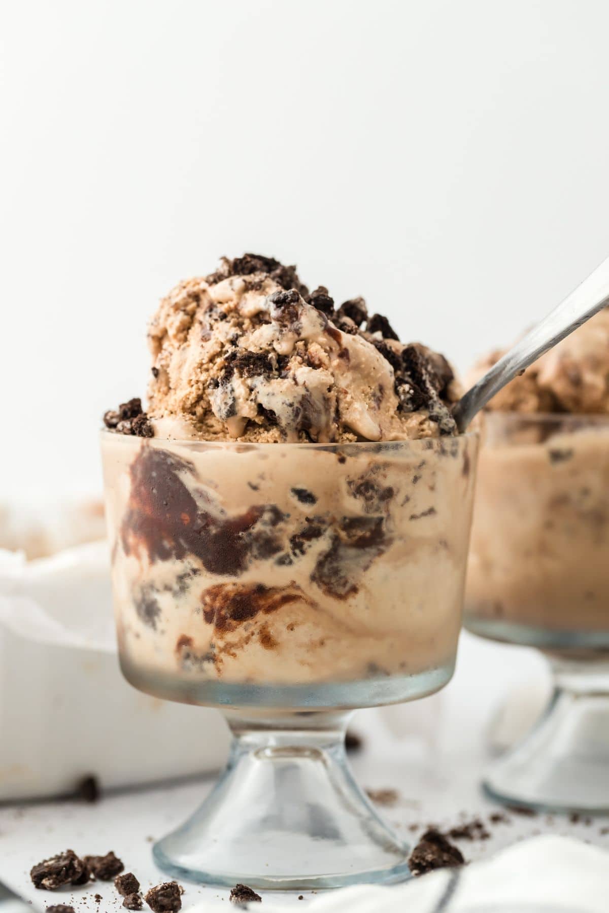 Small glasses filled with scoops of fudge mocha ice cream on the table with a spoon in the glass in the front.