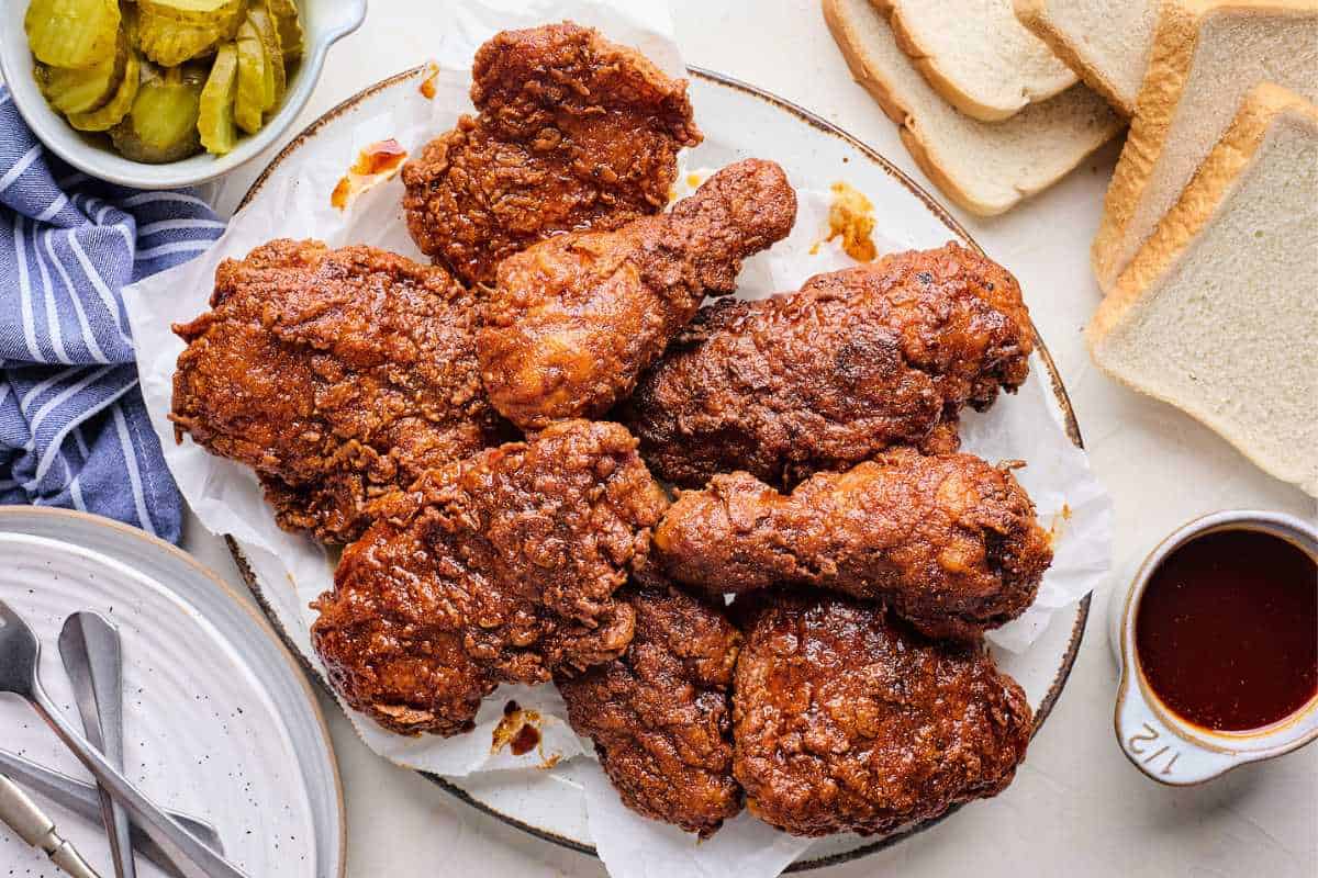 Nashville Fried Chicken being brushed with a Hot Chicken glaze over white bread and pickles