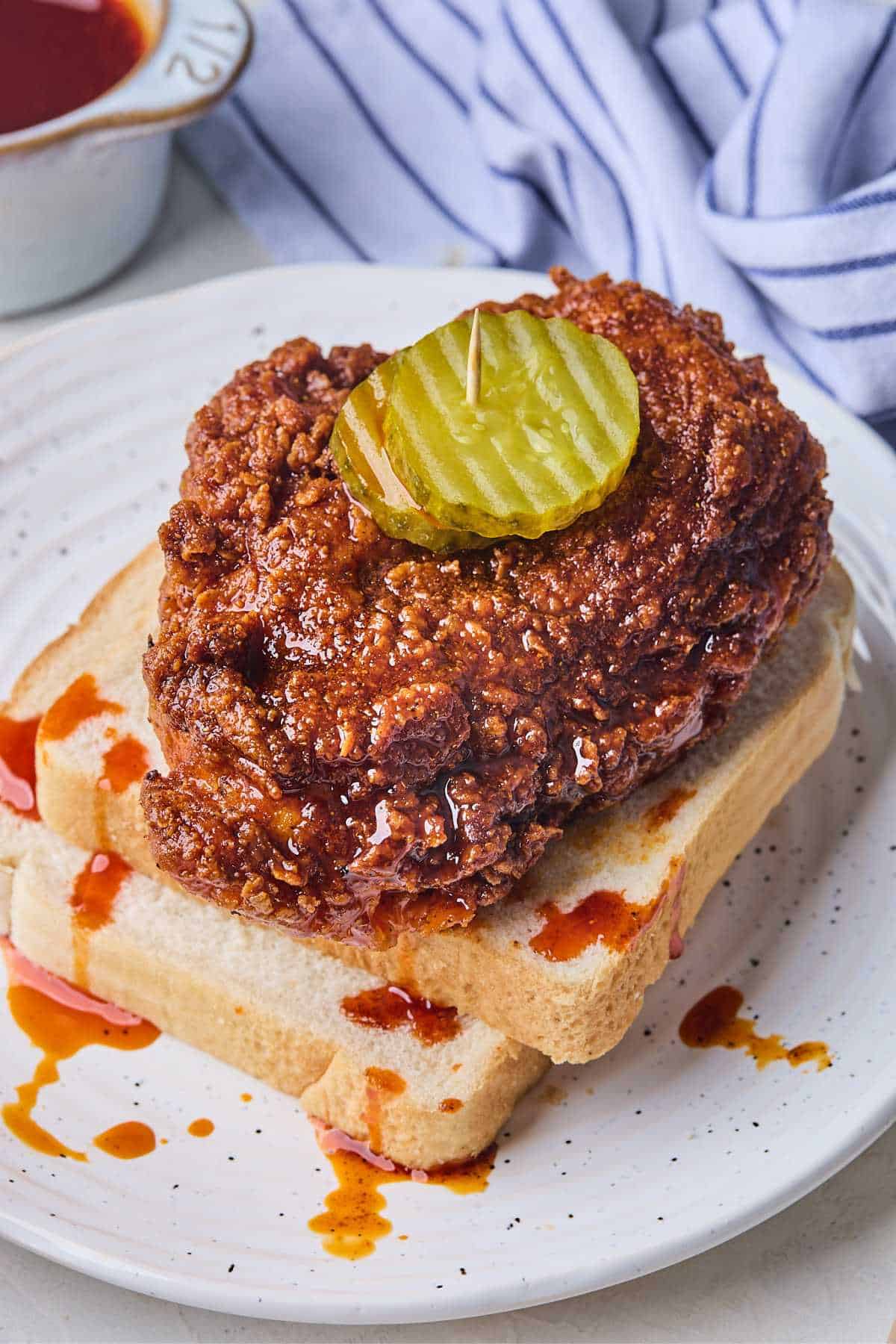 Nashville Hot Chicken over white bread topped with pickles on a white plate.