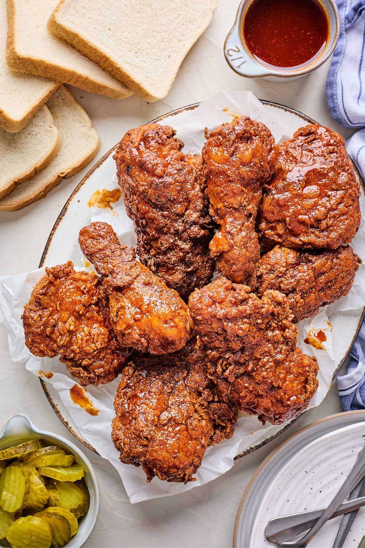 An overhead shot of Hot Chicken on a platter with slices of white bread and a pitcher of sauce to the side.