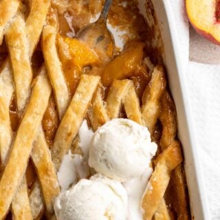 Southern Peach Cobbler Recipe with spoon removing some and two scoops of vanilla ice cream on top on white background