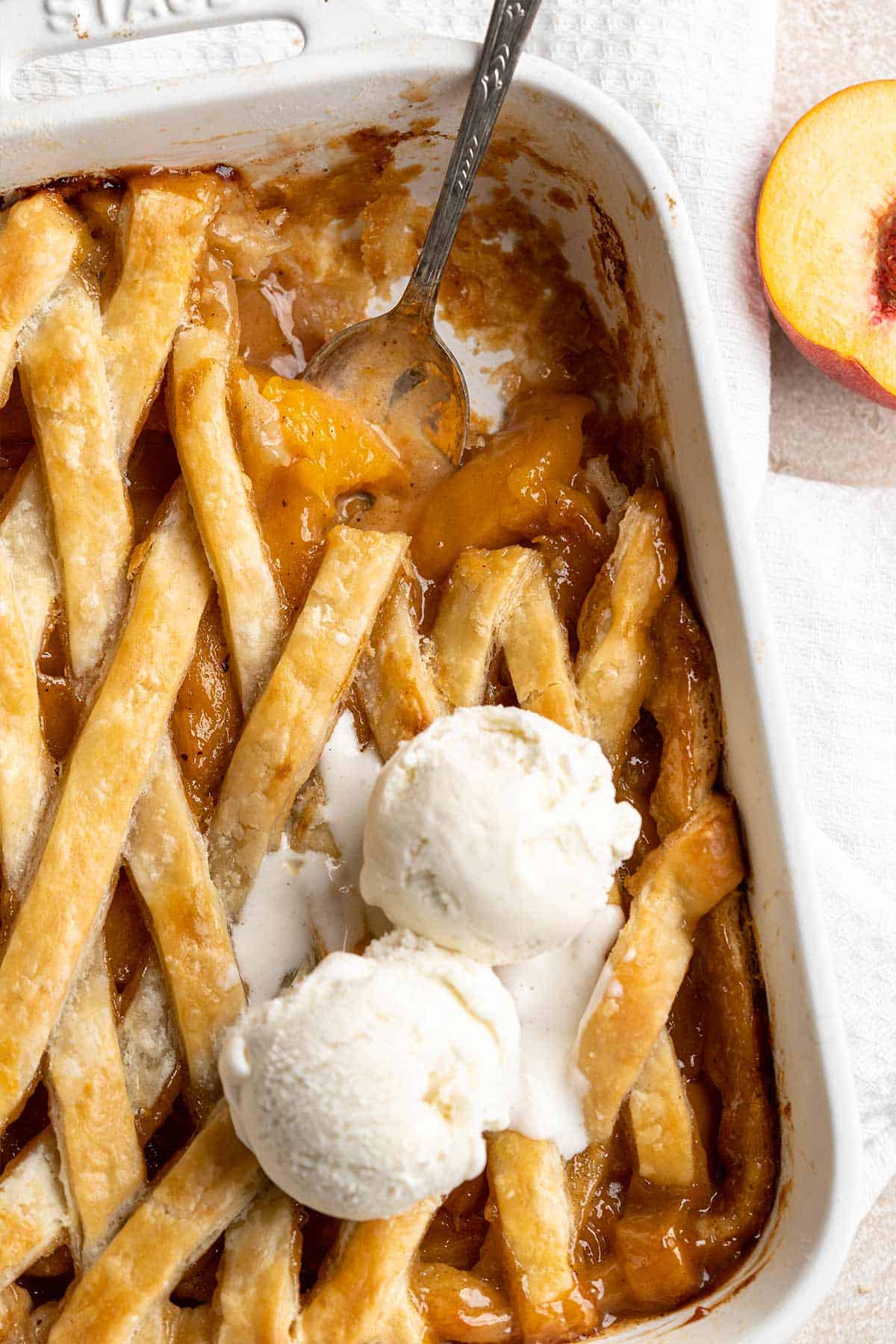 Peach cobbler with canned peaches in a baking dish with a portion missing and the spoon in the dish.