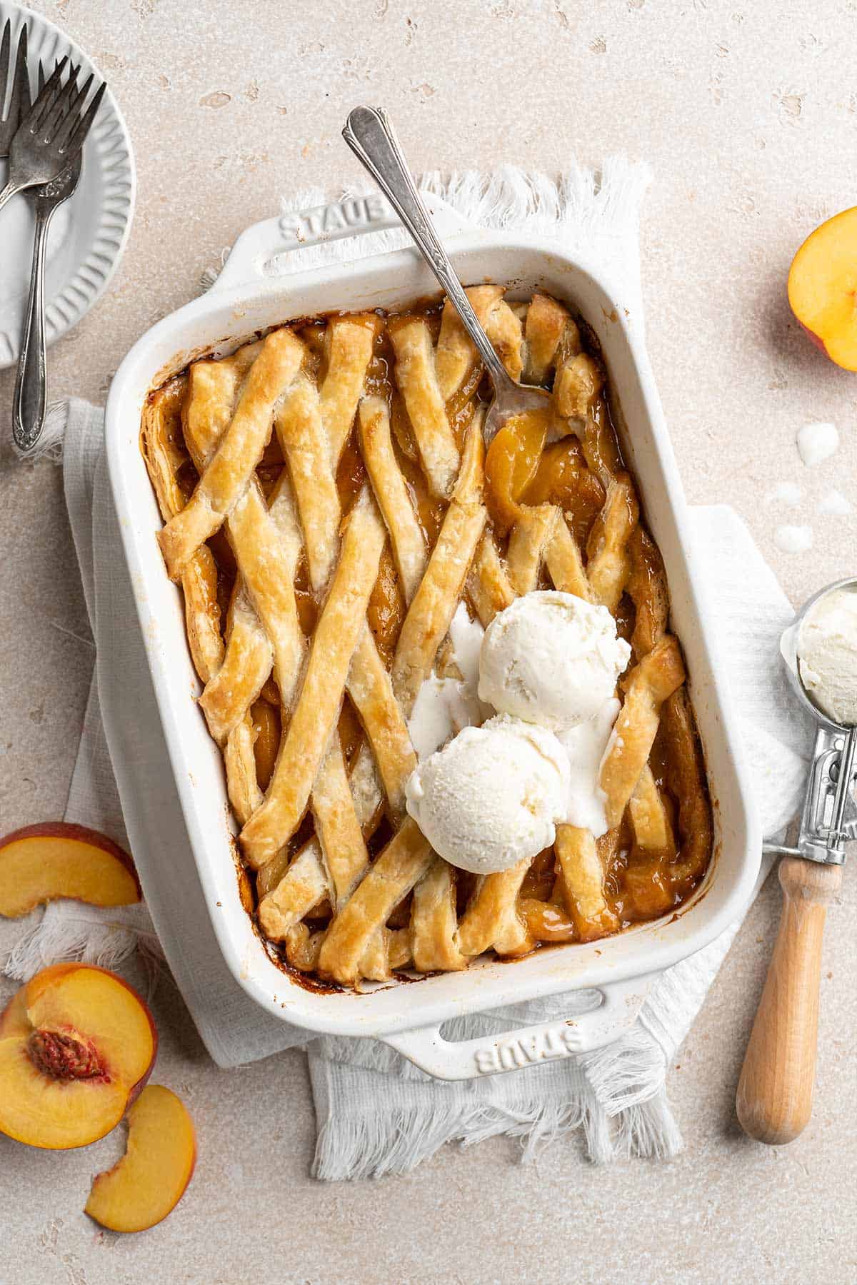 Southern peach cobbler with canned peaches served up in a casserole dish with a spoon digging into it and two scoops of ice cream on top.