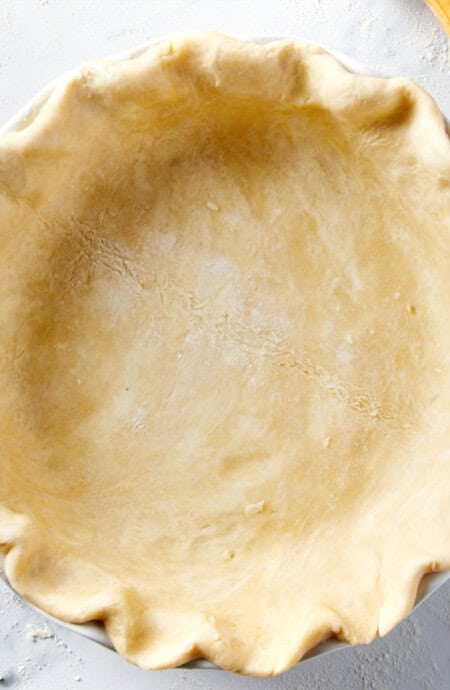 A perfect pie crust in a pie plate on the table with flour sprinkled around.
