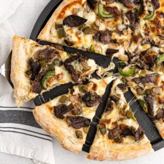 A philly cheesesteak pizza on the pan with slices cut and slightly pulled out.