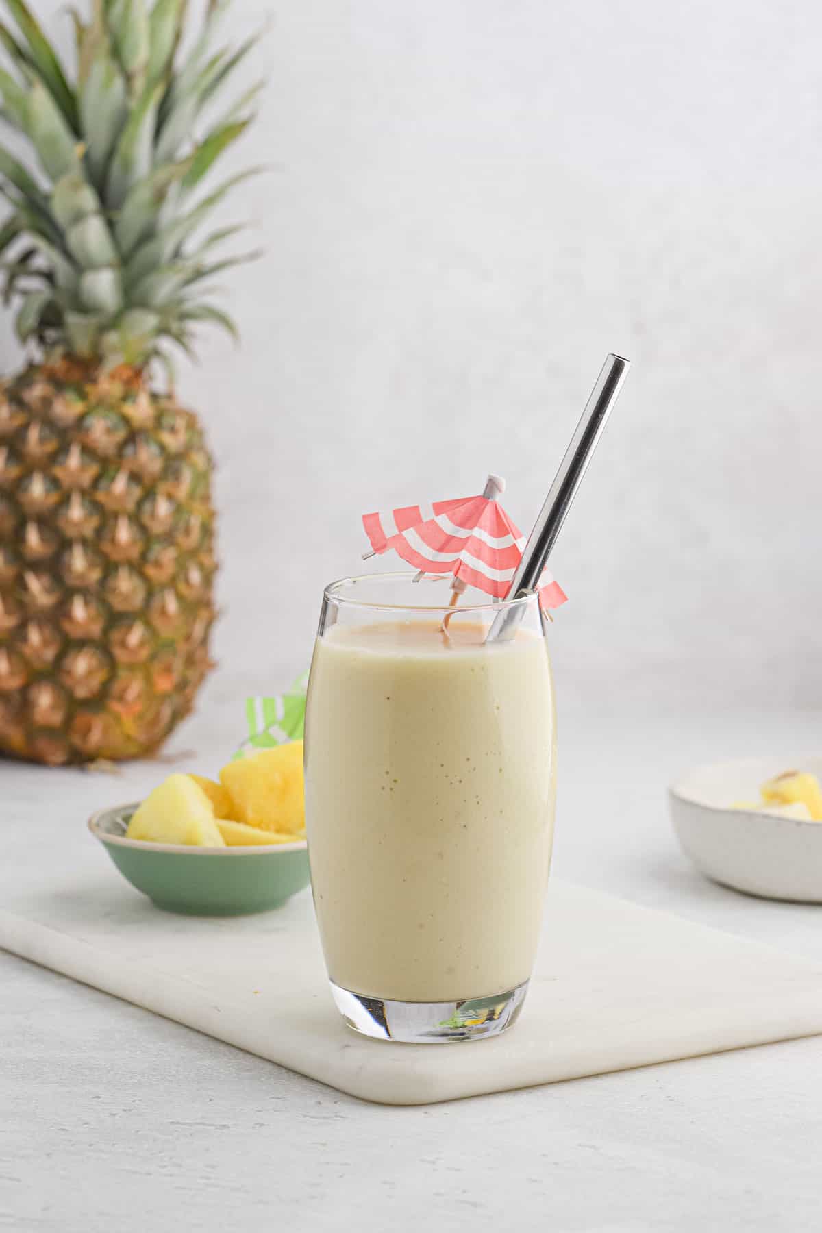 Pina colada smoothie in a glass with a pineapple in the background.