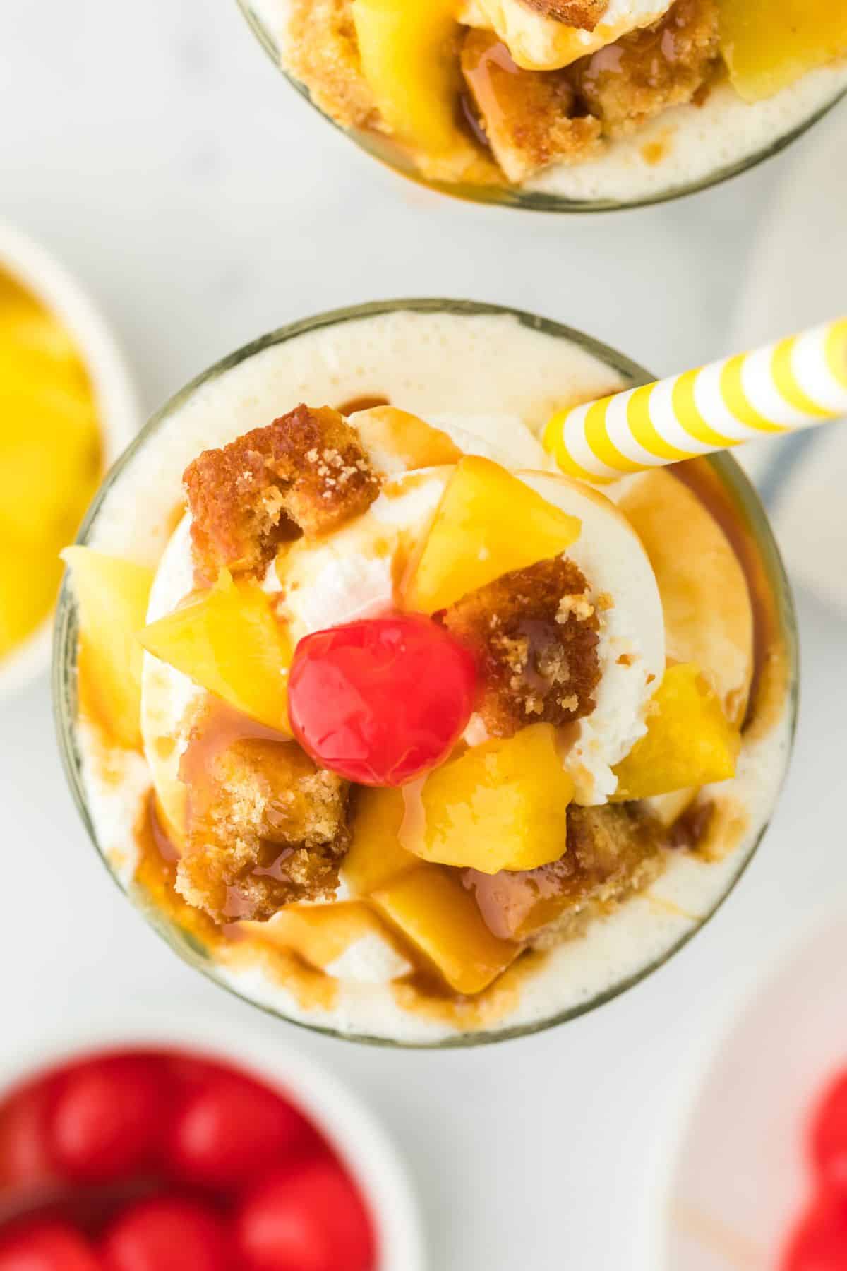 A pineapple shake topped with cake, pineapple pieces, and a cherry.