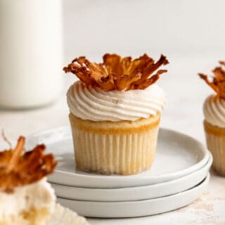 pineapple upside down cupcakes with one on a stack of white plates with milk in a container in white background