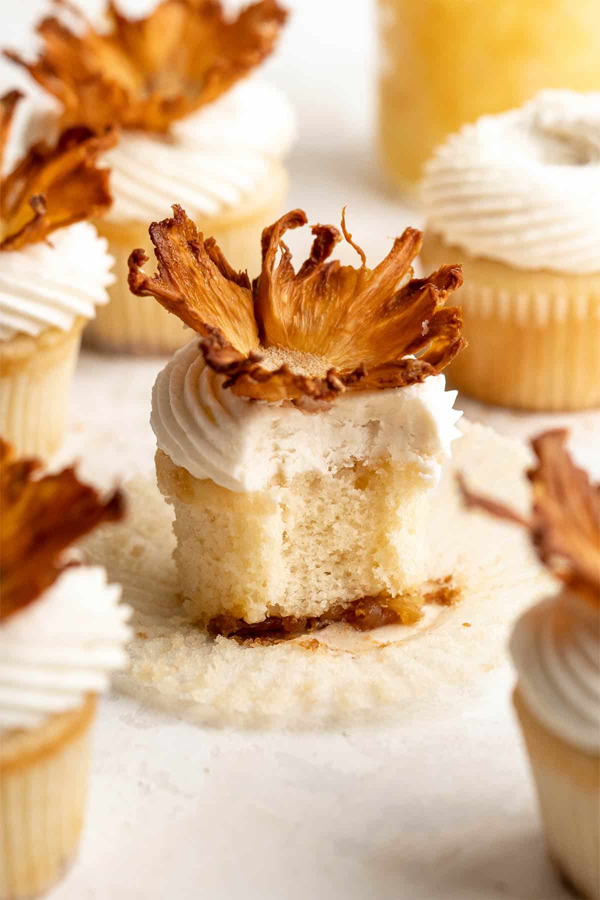 A pineapple upside down cupcake sitting on a piece of paper towel with three others in the background.