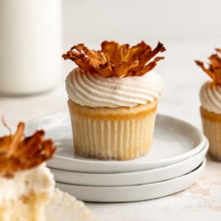 A pineapple upside down cupcake on top of three plates stacked on the table with a few more cupcakes on the edges and a jar of milk in the background.