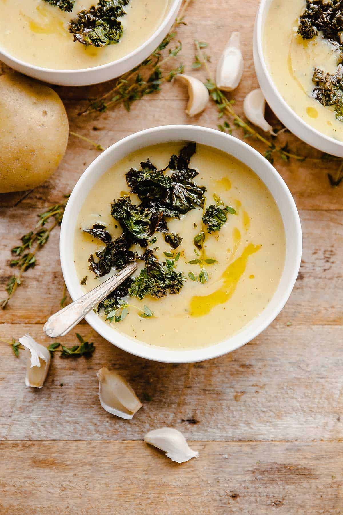 Bowls of homemade potato soup on the table topped with crispy kale.