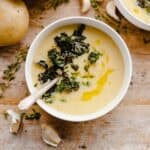 A bowl of potato soup with kale on the table with a spoon in it.