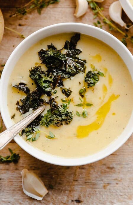 A bowl of potato soup with kale on the table with a spoon in it.
