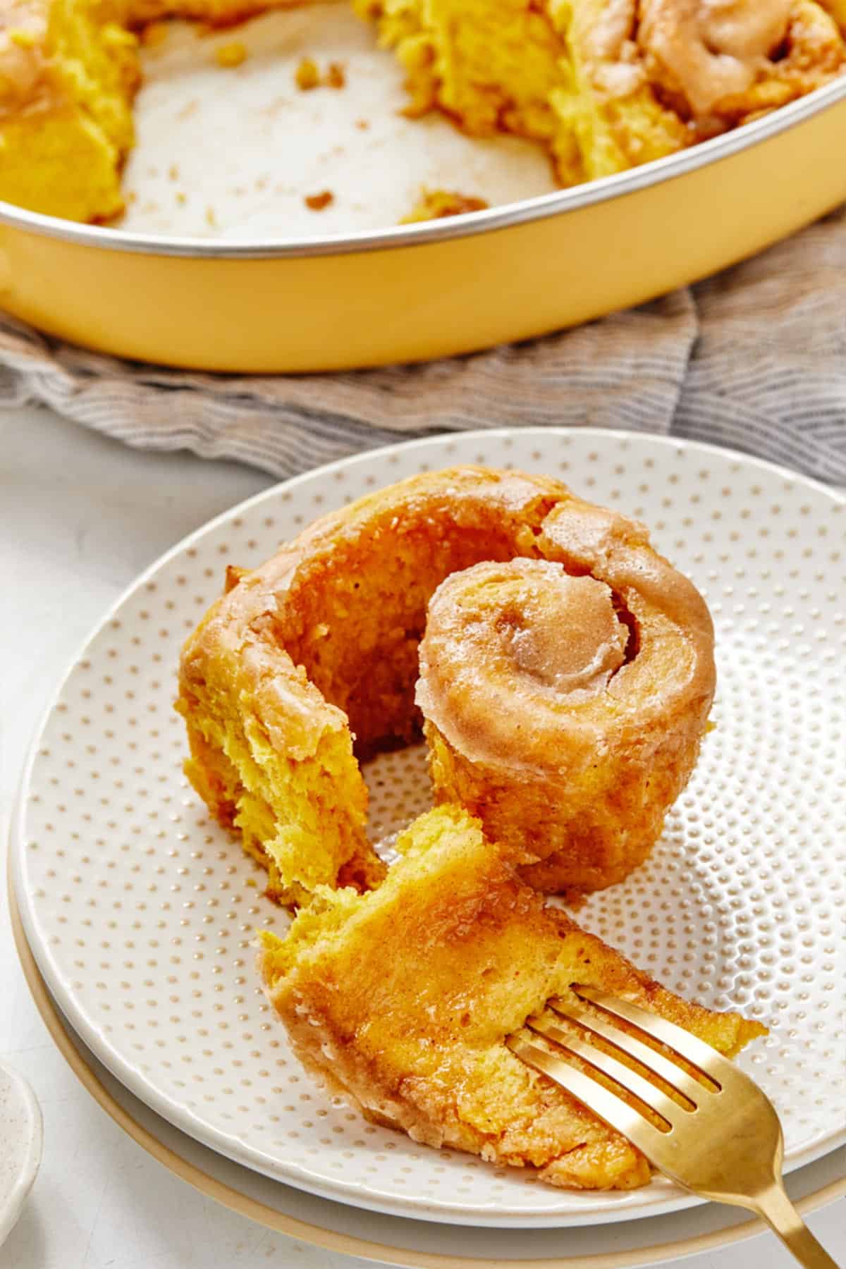 A partially eaten cinnamon roll with pumpkin on a plate with an upside down fork.