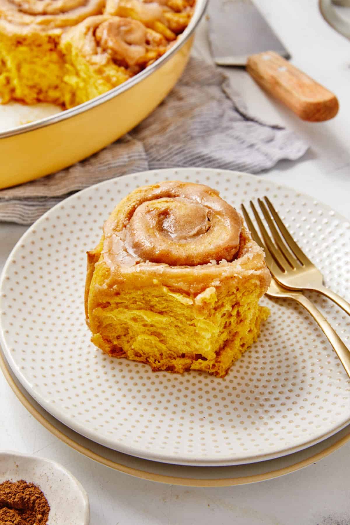 Pumpkin cinnamon roll on a plate with two forks and a pan of more in the background.