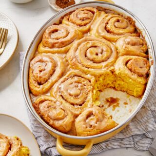 Close up of a pumpkin cinnamon rolls with maple frosting sitting on a round, white plate with a fork