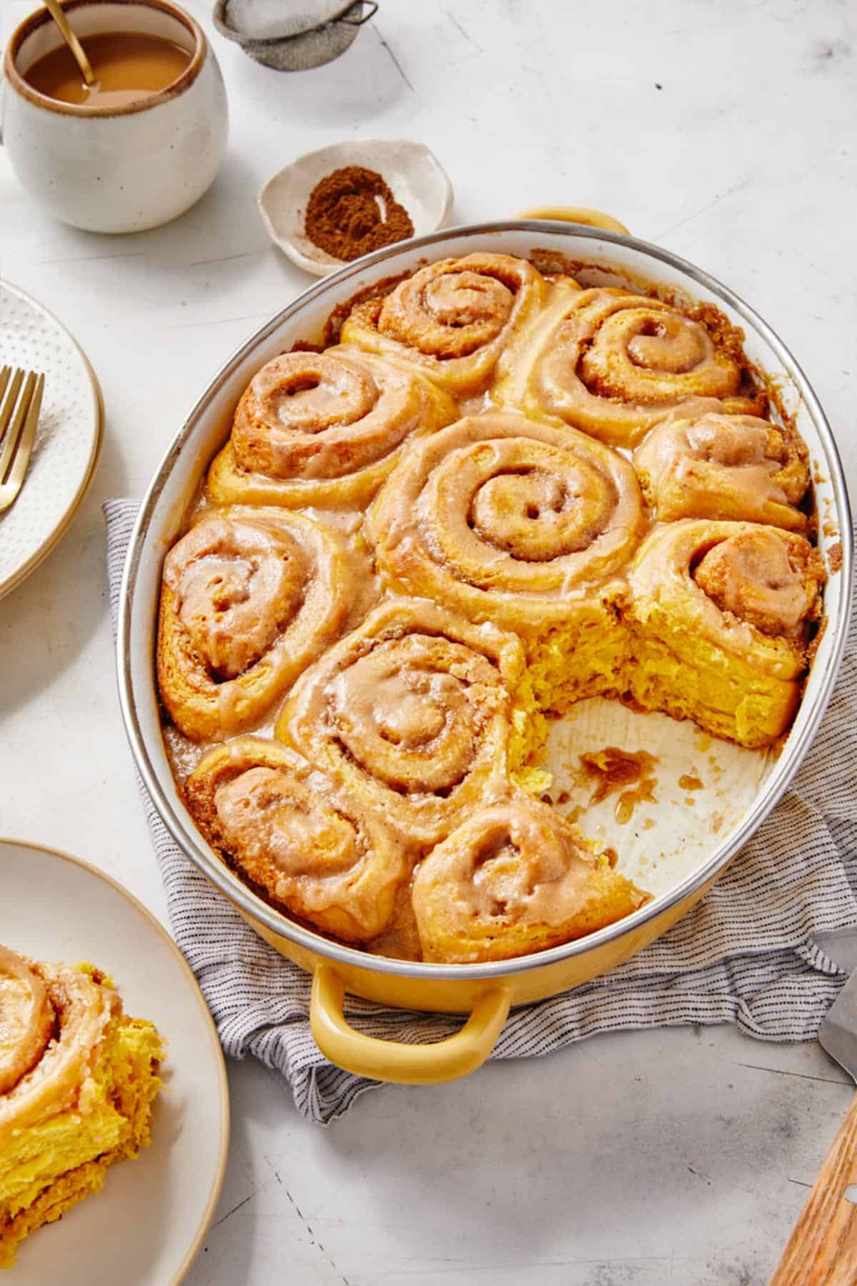 Close up of a pumpkin cinnamon rolls with maple frosting sitting on a round, white plate with a fork