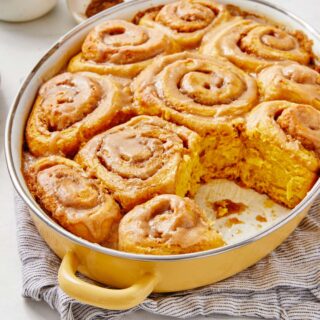 Pumpkin cinnamon rolls in a pan with one missing.