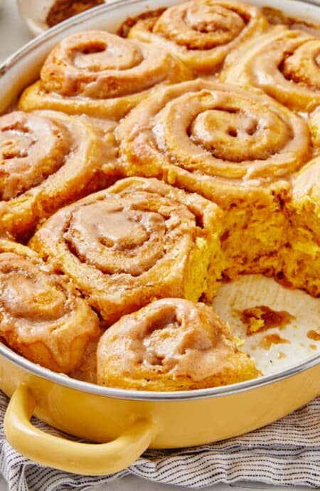 Pumpkin cinnamon rolls in a pan with one missing.