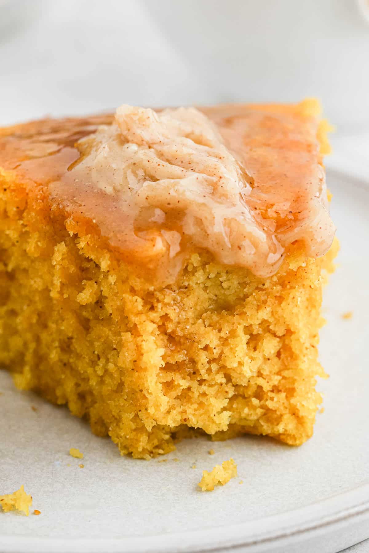 A slice of cornbread with pumpkin  on a plate with cinnamon butter melting on top and a bite missing from the front.